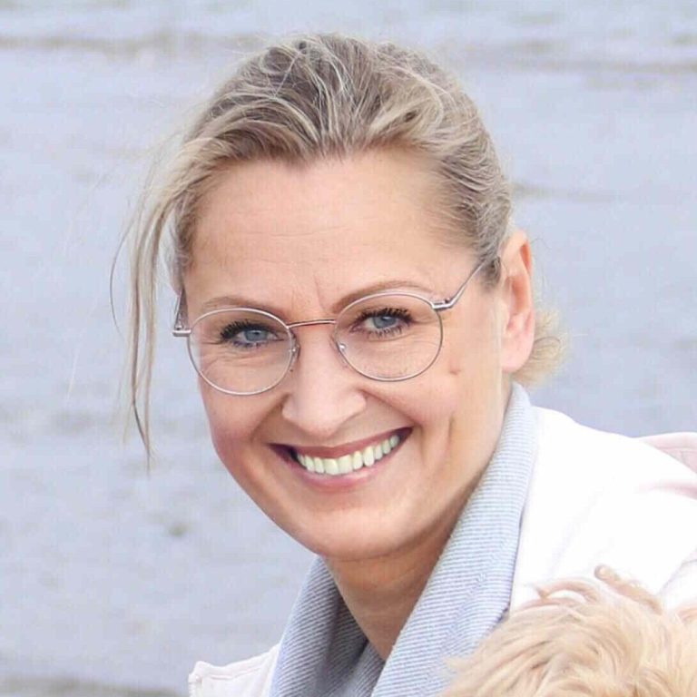 Frau kniet vor einem braunen Hund und lächelt ihm zu.
